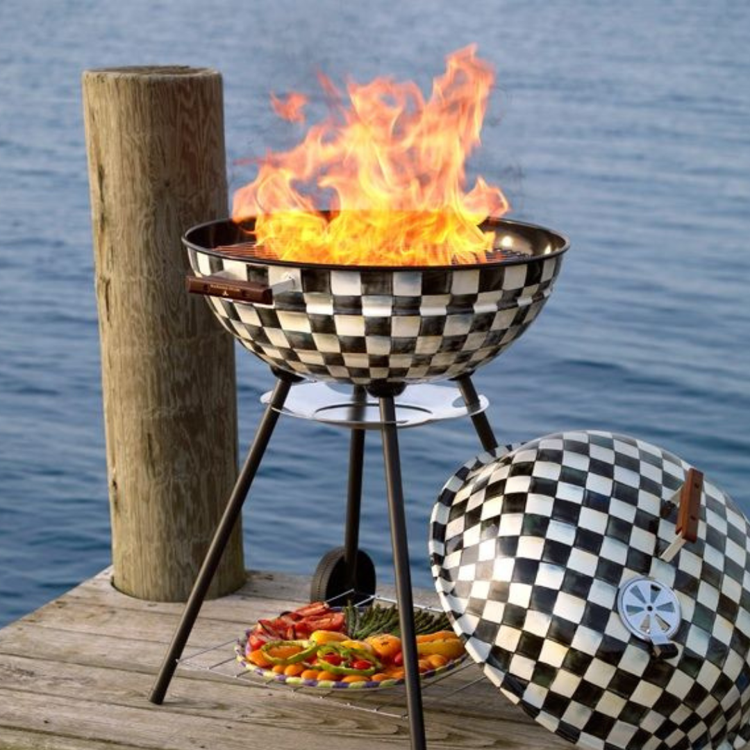 Checkered barbecue grill with flames on a wooden dock by water