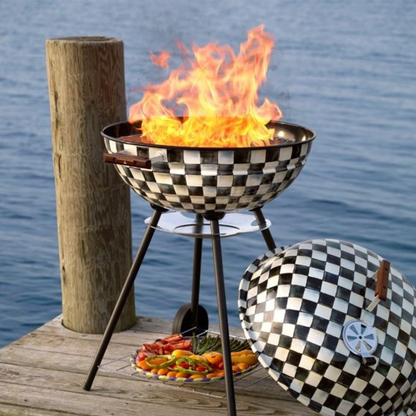 Checkered barbecue grill with flames on a wooden dock by water